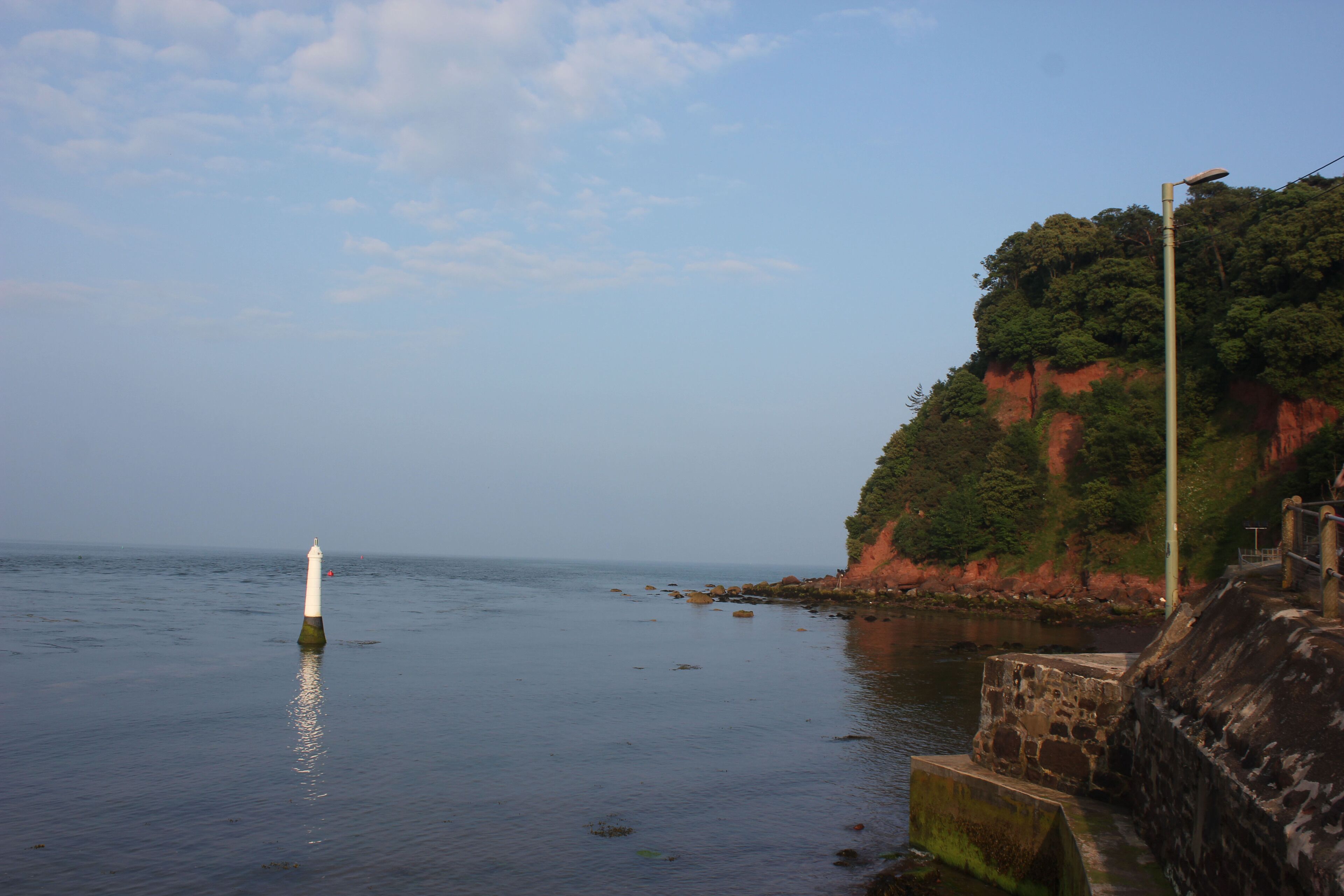 A lighthouse by a calm sea with a rocky cliff in the background.