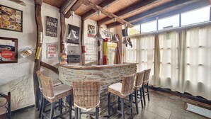 Um espaço de bar rústico com cadeiras de vime, balcão de pedra e diversos objetos de recordação nas paredes.