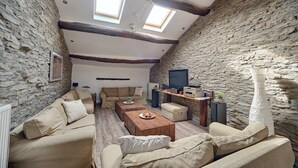 Uma sala de estar acolhedora no estilo loft, com paredes de pedra, teto de madeira e TV integrada.