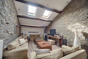 Un accogliente soggiorno mansardato con pareti in pietra, soffitto in legno e TV a incasso.