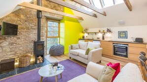 A cozy living room with a stone fireplace, a bright yellow accent wall, and a modern kitchen with wooden beams. - Rural chic - The Hayloft others style and comfort with a rustic charm. (Balerno)