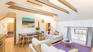 A spacious living area with a high ceiling, exposed wooden beams, a dining table with chairs, a sofa, a coffee table, and a bookshelf. - Rural chic - The Hayloft others style and comfort with a rustic charm. (Balerno)