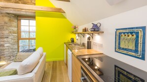 A compact kitchen with a bright yellow wall, a stone wall, and a wooden ceiling. It includes a sink, a stove, and a small shelf with decorative items. - Rural chic - The Hayloft others style and comfort with a rustic charm. (Balerno)