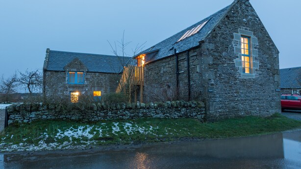 A stone building with a steeply pitched roof, a visible window with blue trim, and a stone wall in front. - Rural chic - The Hayloft others style and comfort with a rustic charm. (Balerno)