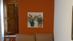 A room with an orange wall, a bed with beige bedding, a wooden door, and a small table with a lamp. - German house at the Borgo (Badolato)