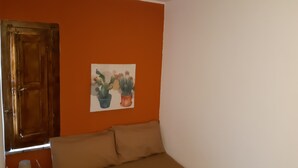 A room with an orange wall, a bed with beige bedding, and a painting of two potted plants. - German house at the Borgo (Badolato)