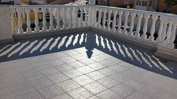 Een betegeld balkon met een witte balustrade, met uitzicht op een woonwijk met huizen en een heldere lucht.