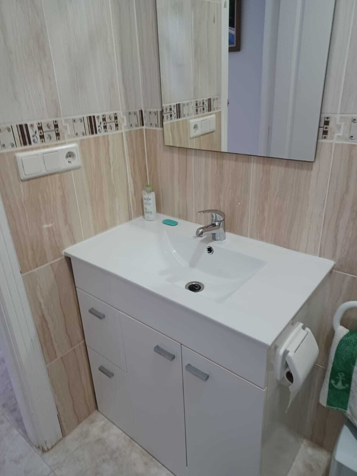 A bathroom with a white sink, a mirror above it, and a toilet to the right. There are cabinets below the sink and a towel hanging on the wall.