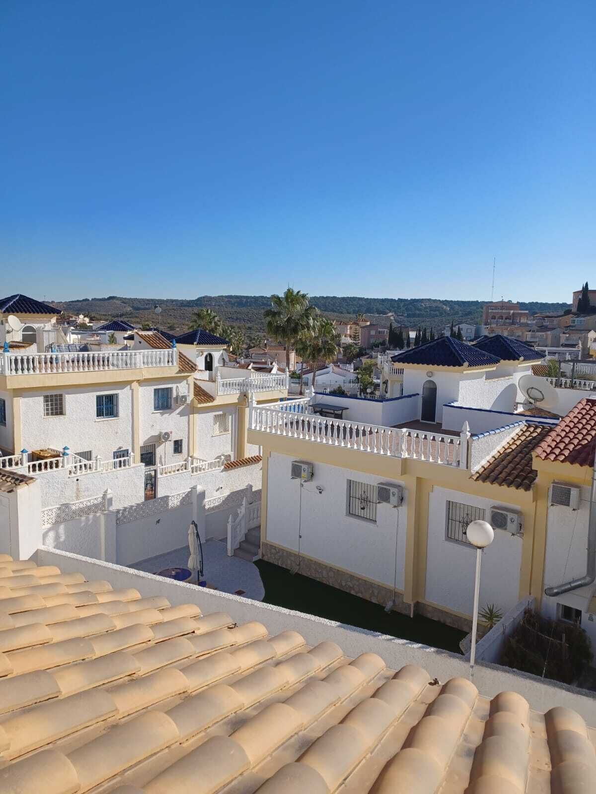 A residential area with white buildings, a clear blue sky, and a view of distant hills.
