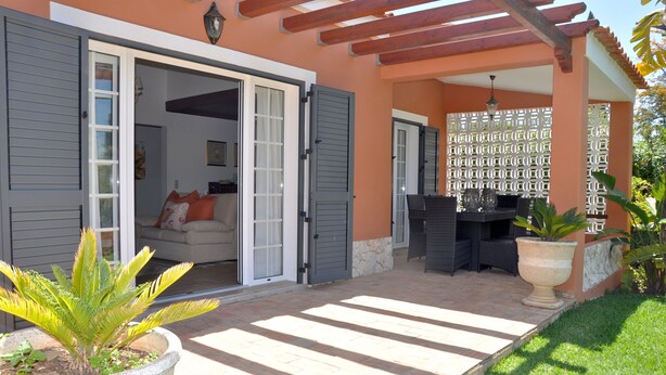 Ein überdachter Patio-Bereich mit einer Sitzecke und einem großen Pflanzgefäß.