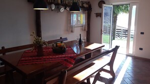 A dining area with a wooden table, benches, and a red patterned tablecloth. There are hanging lights, a shelf with bottles, and a window with a view of the outdoors. - Villa with large garden and super breathtaking panorama, relaxation, peace (vercana)