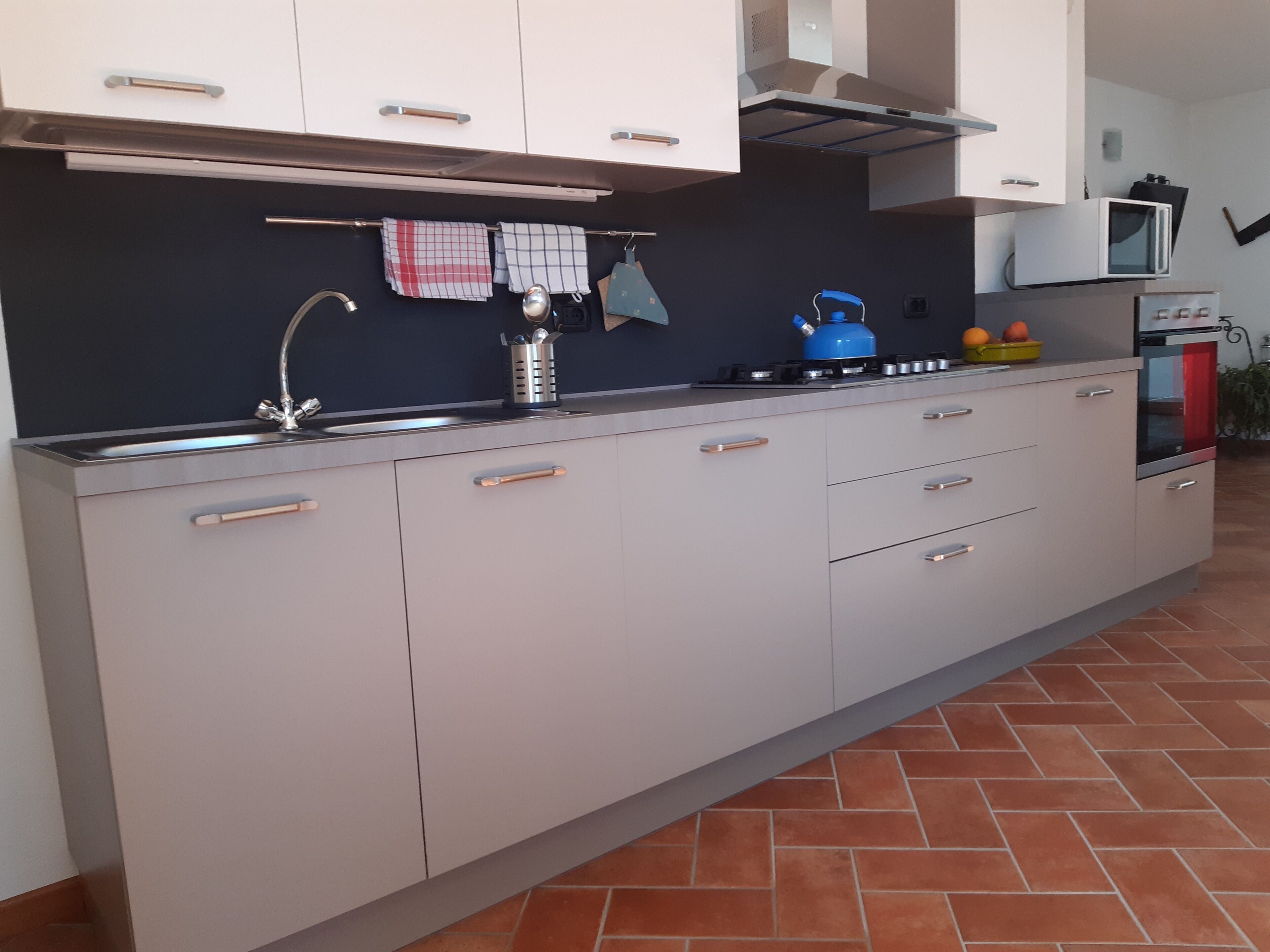 Una cocina moderna con un lavamanos de acero inoxidable, un hervidor azul y un microondas.