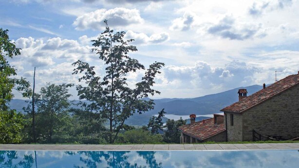 Una piscina con vista chiara su un paesaggio montuoso e un edificio in pietra con tetto in tegole.