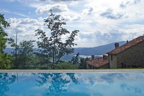 A swimming pool with a clear view of a mountainous landscape and a stone building with a tiled roof.