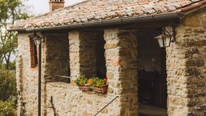 Un edificio in pietra con tetto in tegole, una scala che conduce a una porta e un’ampia finestra con un vaso fiorito.