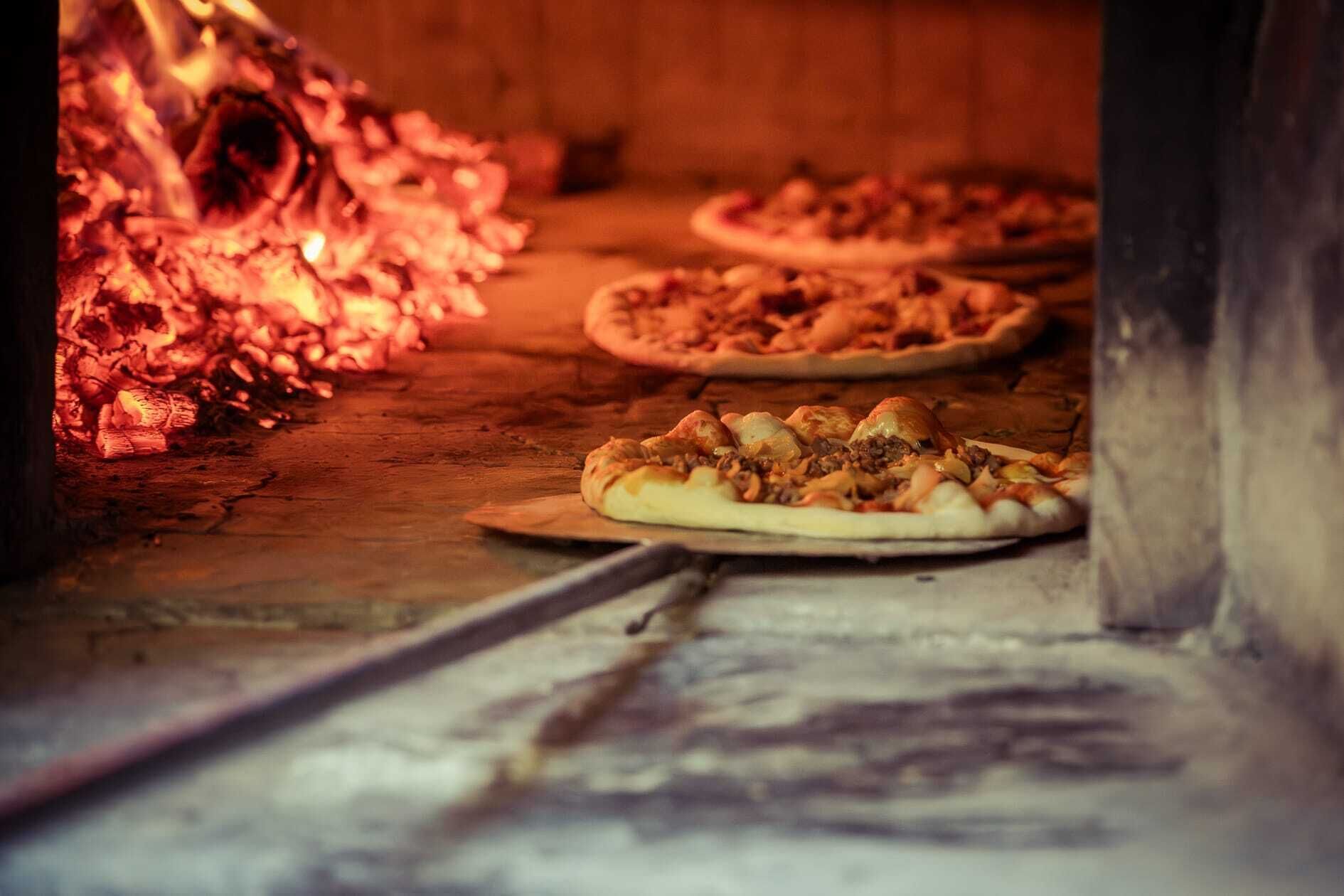 A wood-fired oven with pizzas baking inside.