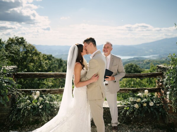 A couple kissing at a wedding ceremony with a scenic view in the background.