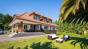 A two-story house with a tiled roof, a covered porch, and a well-maintained lawn. - Elegant country house with pool. Between Oviedo and Gijón (Siero)
