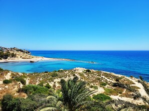 Paisatge costaner amb platja, terreny rocos i vegetació escassa.