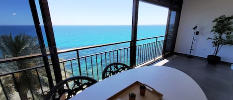 A balcony with a view of the sea, a table with a tray of items, and a potted plant.