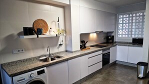 Een moderne keuken met witte kasten, een granieten aanrecht, een ingebouwde wasmachine en een raam met decoratieve screen.