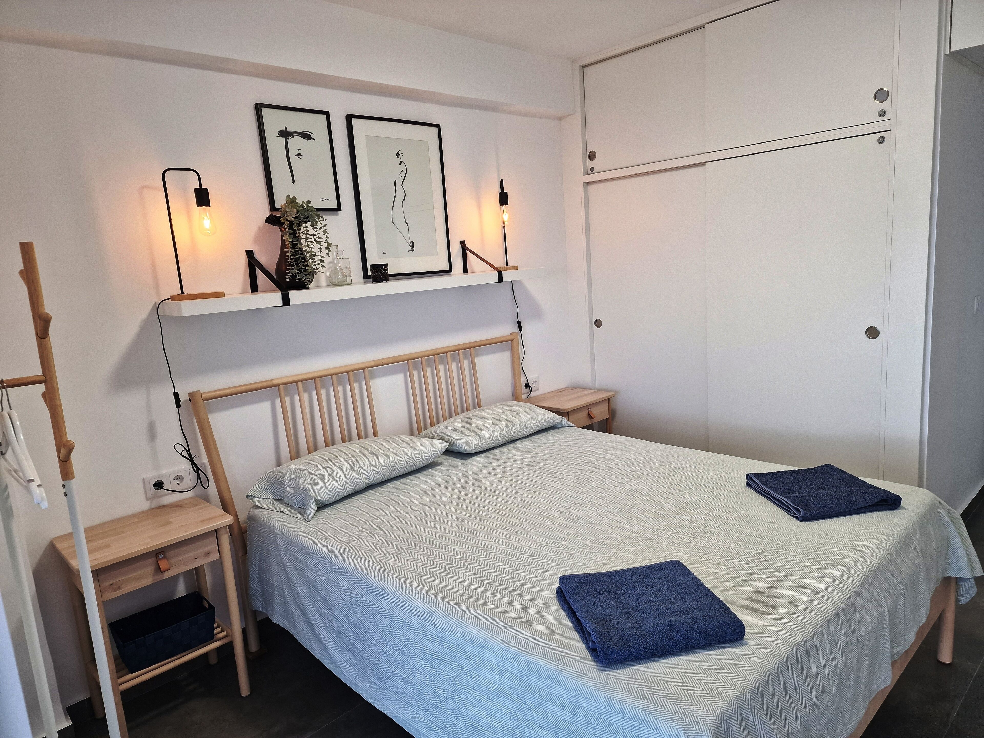 Une chambre bien rangée, avec un lit, des tables de chevet, une armoire et des œuvres d’art accrochées au mur.