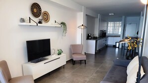 Een moderne woonkamer met een flatscreen televisie, een bank, een stoel en een eethoek op de achtergrond.