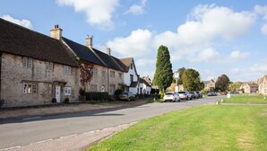 A street with stone buildings, parked cars, and a grassy area. - Charming Country House Nr Bath (WC) (Biddestone)