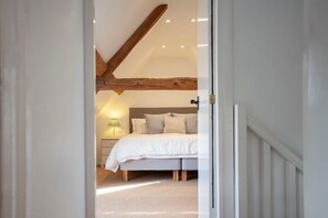 A bedroom with a bed, bedside table, lamp, and a wooden beam ceiling.