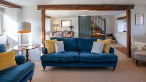 A living room with a blue sofa, a round table, and a lamp. There is a staircase in the background leading to another level. - Charming Country House Nr Bath (WC) (Biddestone)