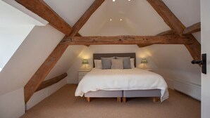 A bedroom with a sloped ceiling, wooden beams, a bed with pillows, a nightstand, and a lamp. - Charming Country House Nr Bath (WC) (Biddestone)