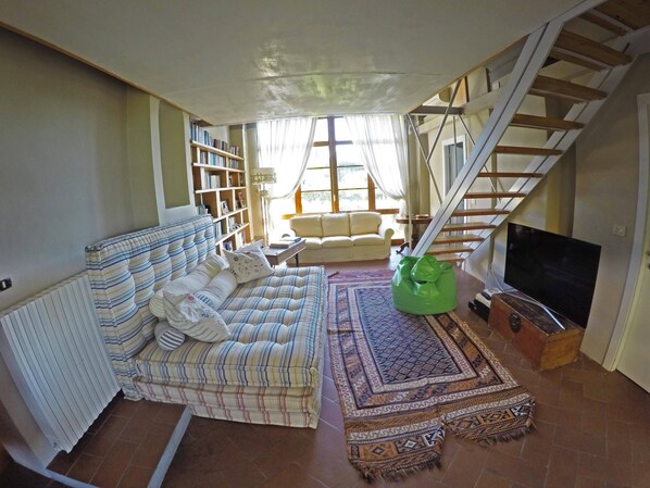 Un salon avec un canapé, un fauteuil en forme de haricot vert, un téléviseur, une bibliothèque et un escalier.