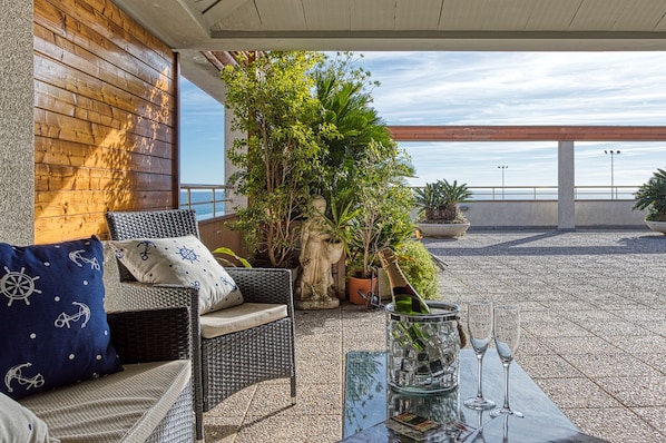 A terrace with wicker furniture, a glass table, and potted plants.