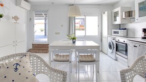 Une cuisine moderne avec des meubles blancs, une table à manger avec des chaises, un lave-linge et un four à micro-ondes.