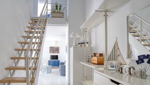 Un intérieur moderne avec un escalier en bois, une console blanche agrémentée d’objets décoratifs et un grand miroir.