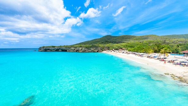 A beach with clear turquoise waters, a sandy shore, and a lush green hill in the background. - *UNIQUE*: Luxury, tropical villa within walking distance of Jan Thiel Beach (6p) (Jan Thiel)