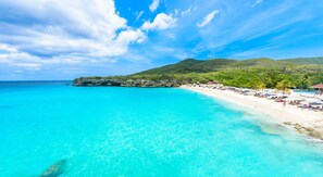 Una playa con aguas turquesas cristalinas, una orilla de arena y una colina verde exuberante al fondo.