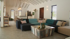 A spacious living room with a large sectional sofa, a coffee table, and a dining area with a wooden ladder and chairs. - *UNIQUE*: Luxury, tropical villa within walking distance of Jan Thiel Beach (6p) (Jan Thiel)