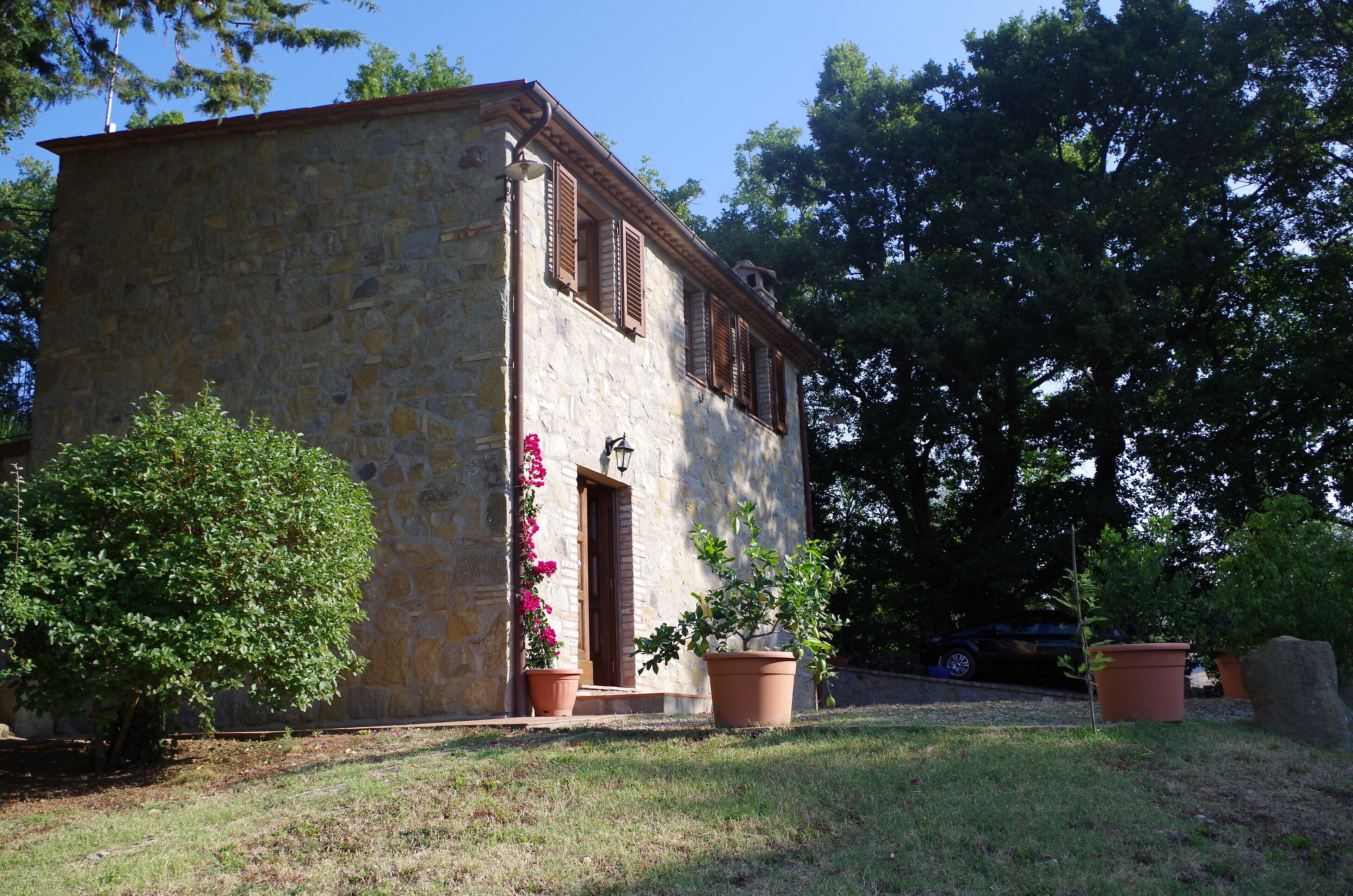 A stone building with a wooden door and shutters, surrounded by potted plants and trees.