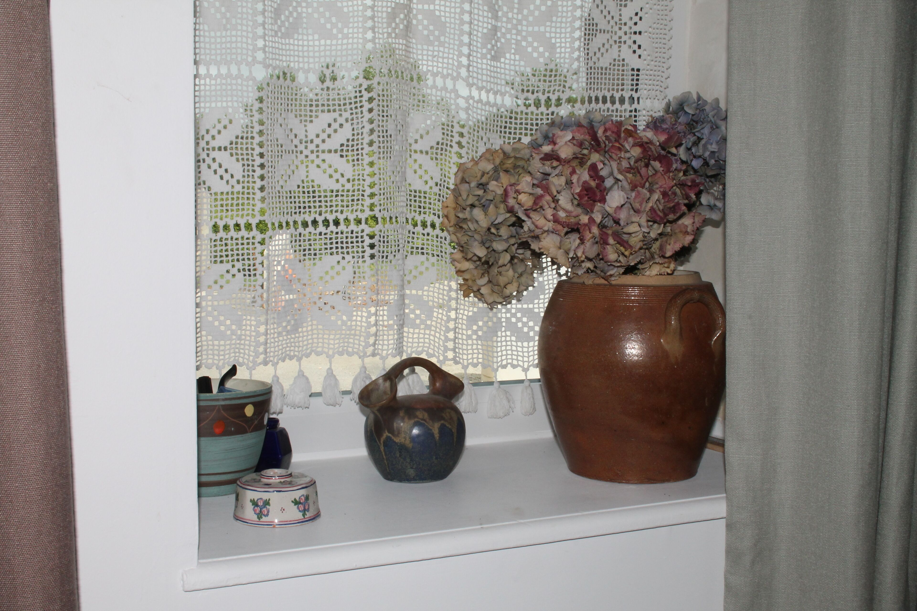 Vensterbank met een grote bloemenvaas, een kleine blauwe theepot en een decoratieve schaal.