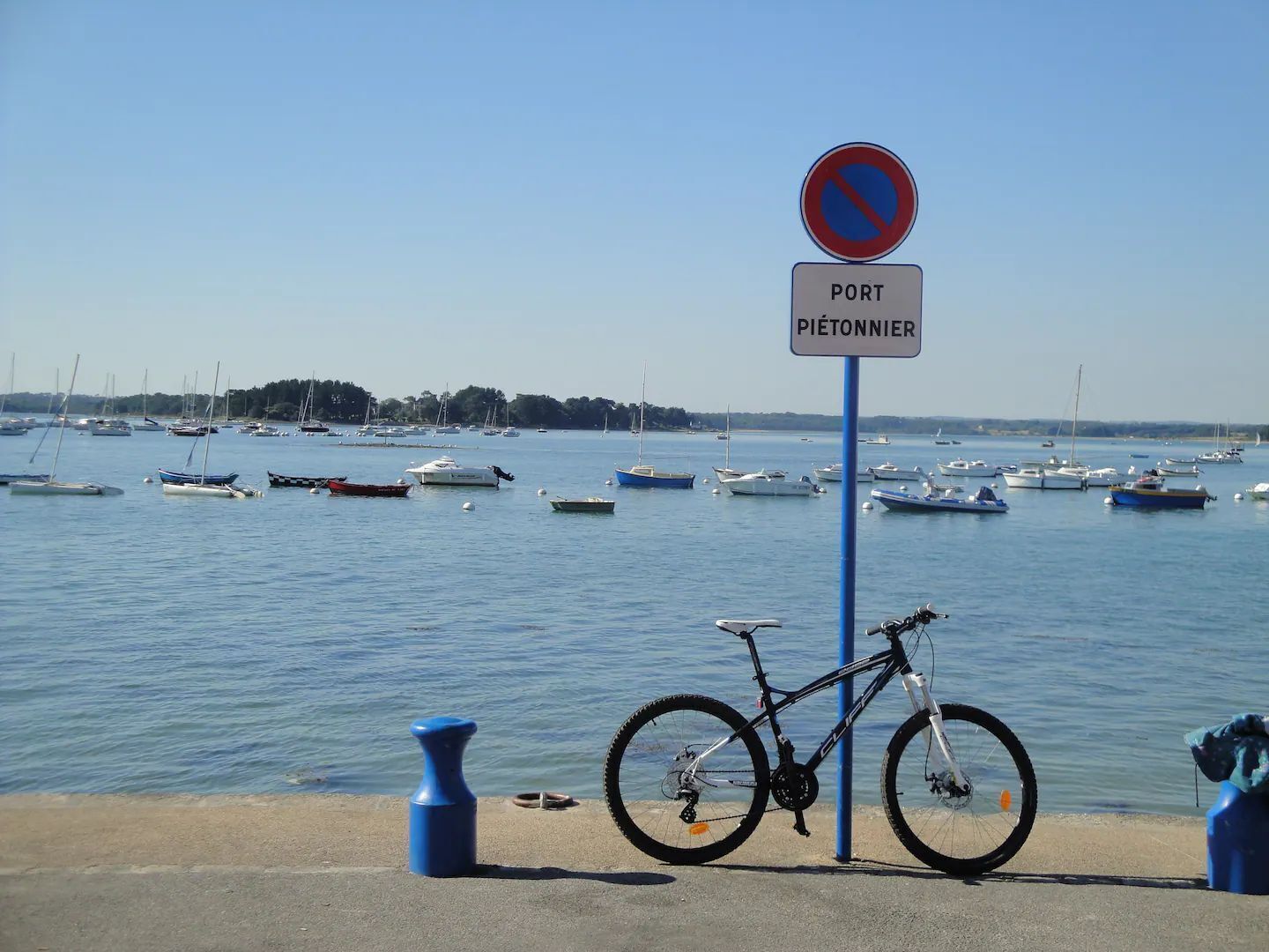 A bicycle parked near a sign with 'PORT PIEDTONNIER' written on it, overlooking a marina with numerous boats.
