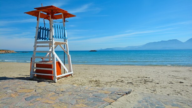 Ein Rettungsturm an einem Strand mit blauem Himmel und ruhigem Wasser.
