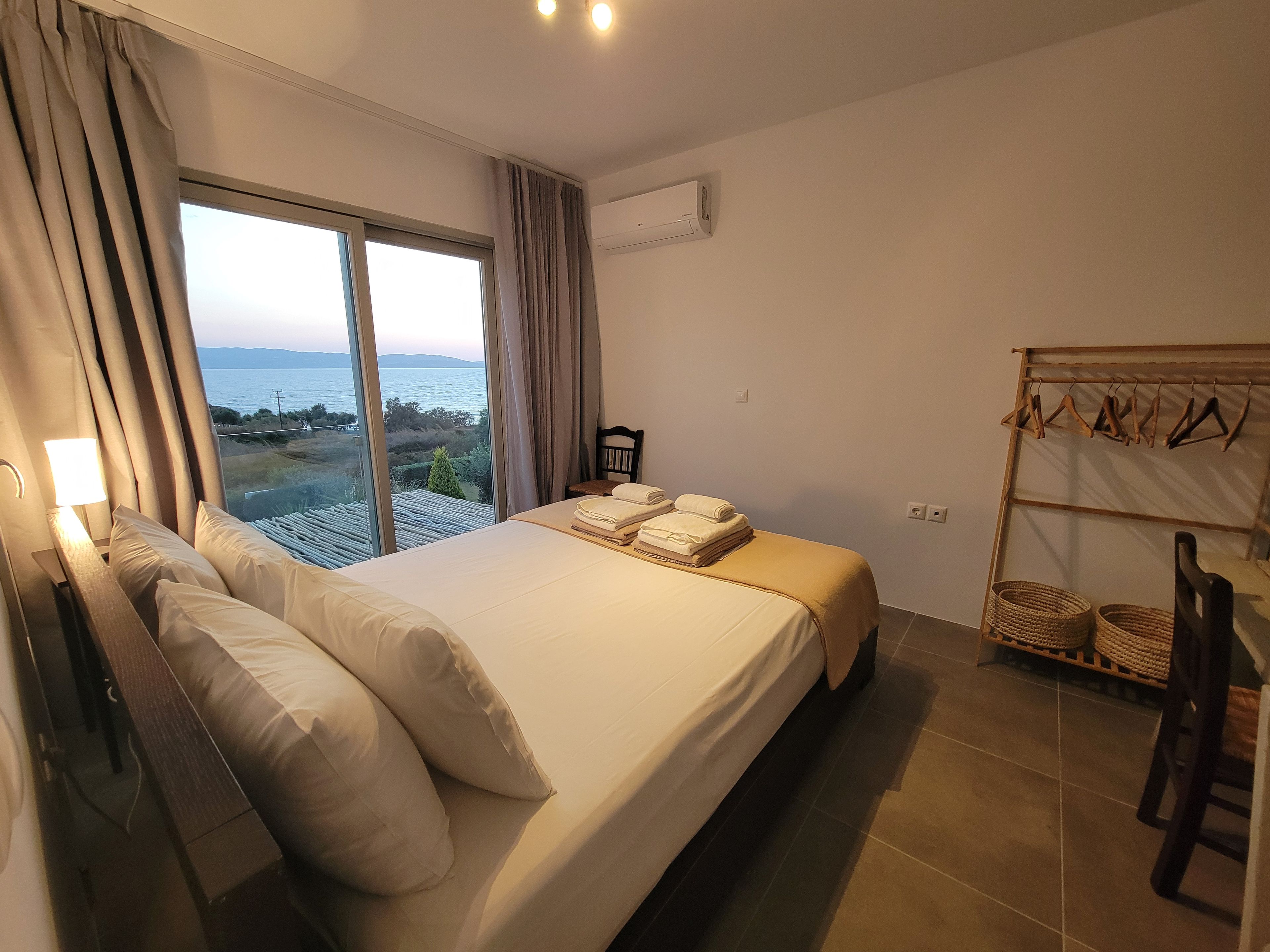 A bedroom with a large bed, a view of the sea, and a drying rack with clothes.