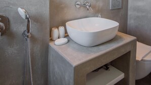 A modern bathroom with a large white sink, a handheld showerhead, and a mirror with built-in lights.