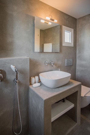A modern bathroom with a large white sink, a handheld showerhead, and a mirror with built-in lights.