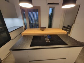 Une cuisine moderne dotée d’un îlot central, d’appareils électroménagers intégrés et offrant une vue par la fenêtre.