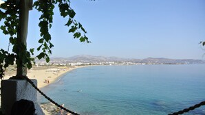 A coastal view with a clear sky, a sandy beach, and a rocky shoreline.