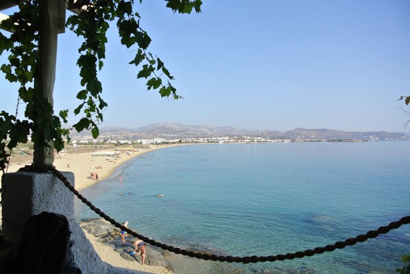 A coastal view with a clear sky, a sandy beach, and a rocky shoreline.