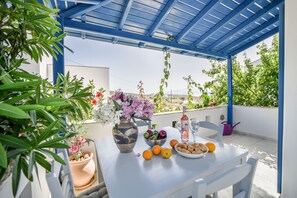 Un espace extérieur aménagé, abrité et doté de tables, prêt pour un repas, et entouré de plantes et de fleurs en pot.
