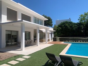 Een modern huis met een zwembad, buitenmeubels en een overdekt terras.